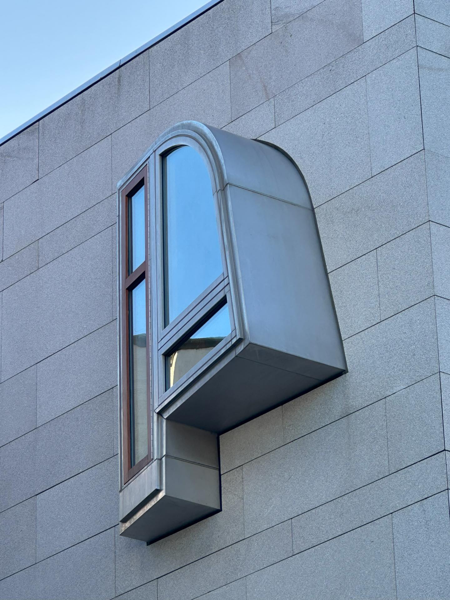 Exterior of tan stone Scottish Parliament building with a protruding p-shaped metal window.