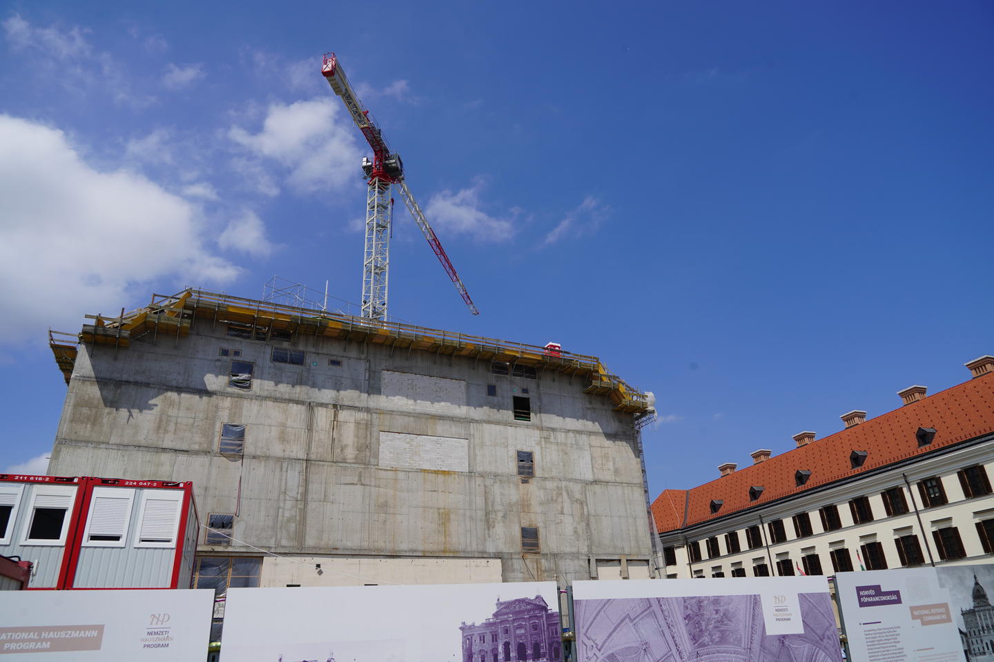 View of Buda castle under construction with a large concrete structure under a large red and white crane and a blue sky.