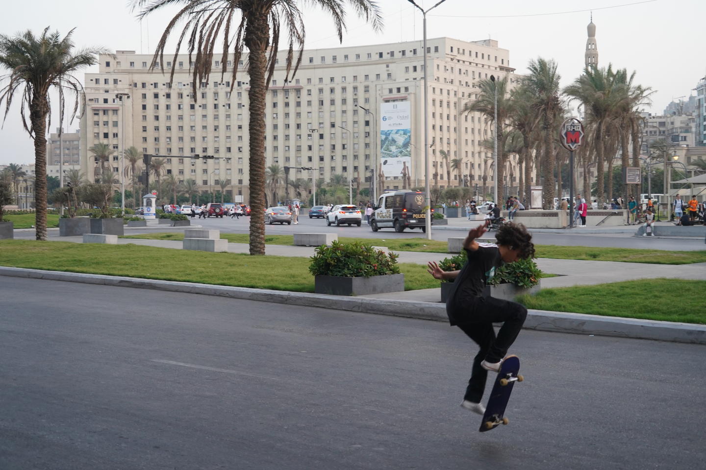 The Mogamma el Tahrir administrative building in Cairo loomd in the background, while a young boy does an ollie on a skateboard in the foreground. 
