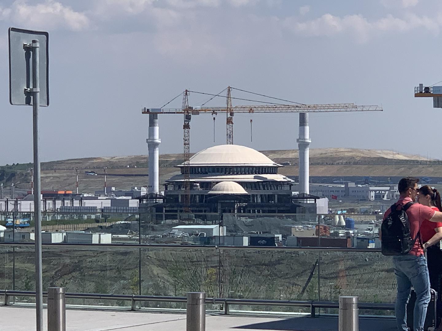 Wide view of the dome and minarets of the under-construction new mosque at the Istanbul airport and giant cranes.