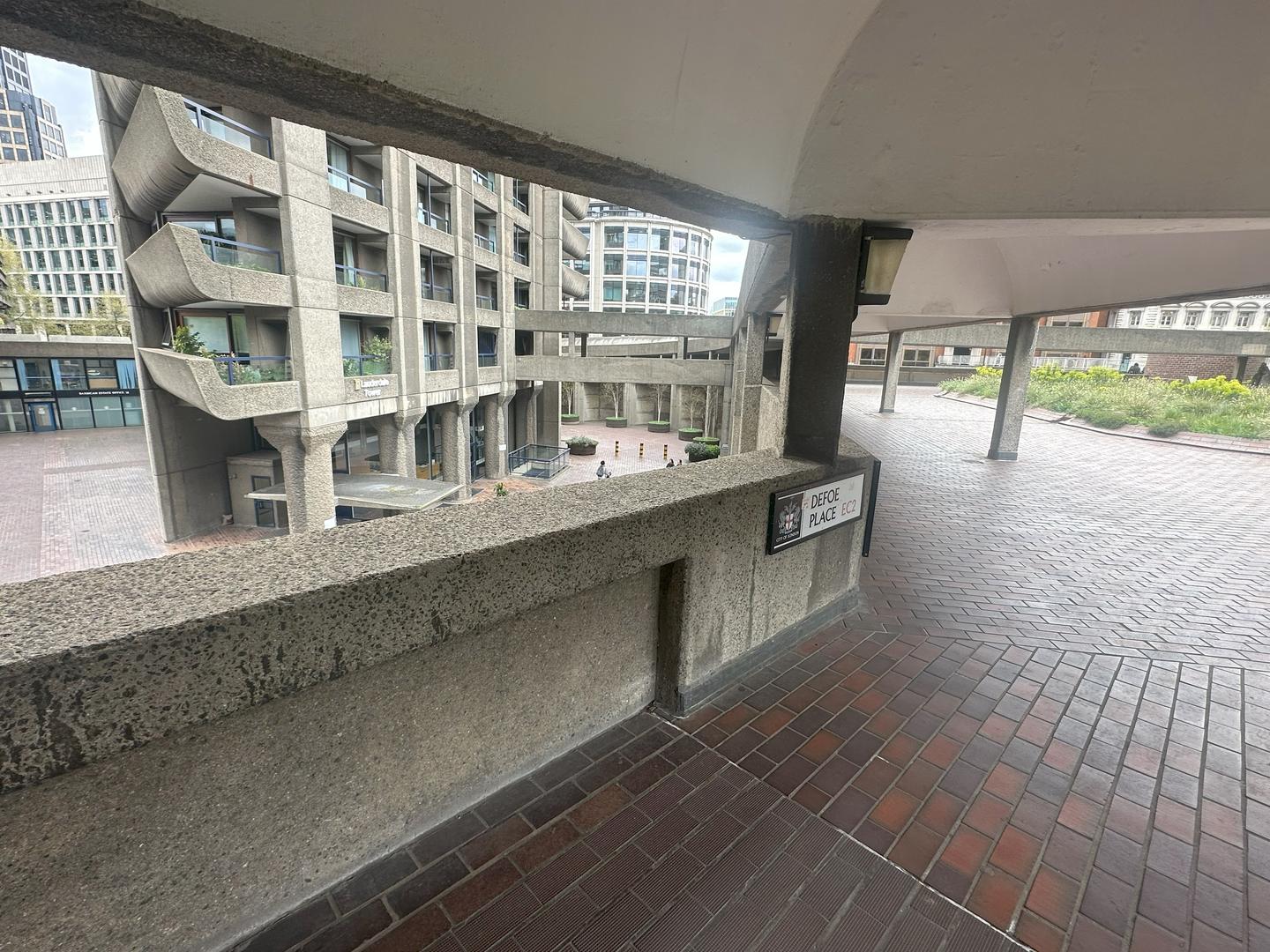 The Brutalist Lauderdale Tower's rough concrete levels are seen through a covered brick walkway in Barbican London.