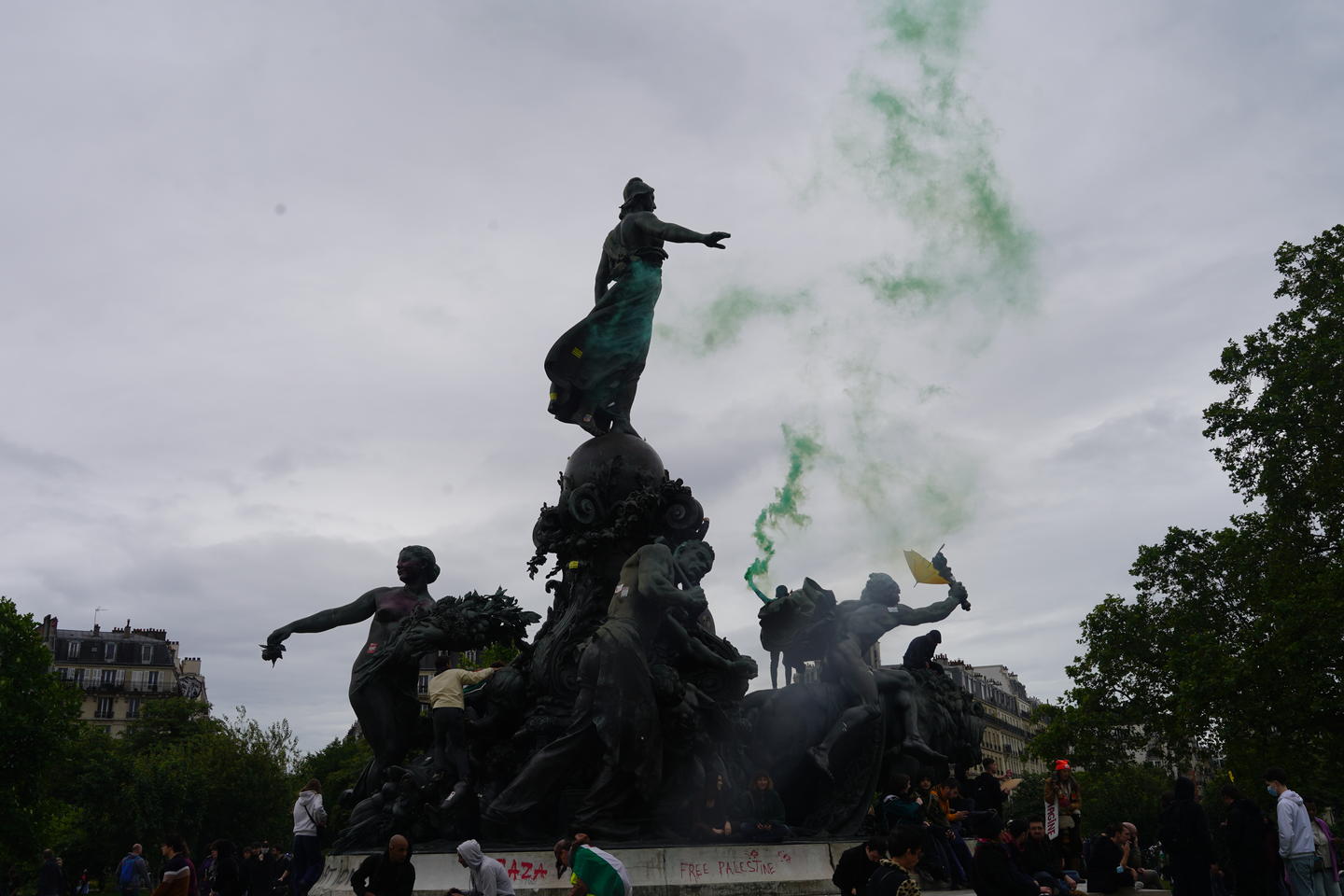 Green smoke rises from the hand of a protester standing on the graffittied "Triomphe de la Republique" statue, in front of which gather protesters during protests of the Israel-Palestinian War in 2024.